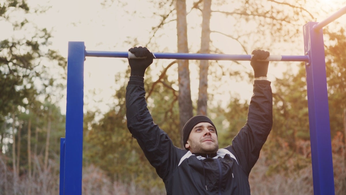 Attractive athletic man doing pull-up exercise in winter park outdoors